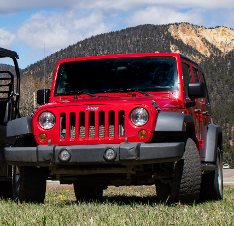 A red jeep parked in the grass near another vehicle.