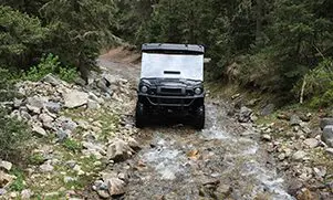 A black atv driving down a trail in the woods.