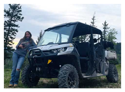 A woman standing next to an atv in the woods.