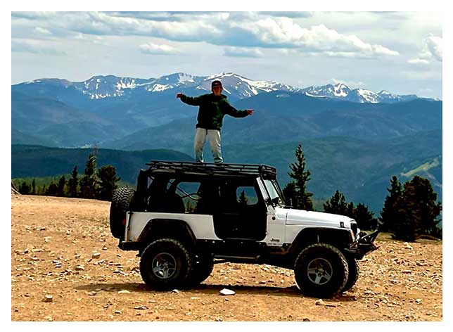A man standing on the hood of a jeep.
